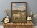 Framed vintage-style painting of two white Brahman cattle in a pasture, displayed on a wicker chest with magnolia flowers.