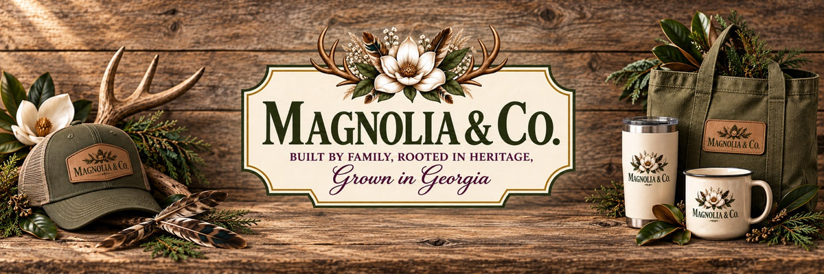 Magnolia & Co. — Built by Family, Rooted in Heritage, Grown in Georgia. Rustic wood display with magnolias, antlers, a hat, tote and drinkware.